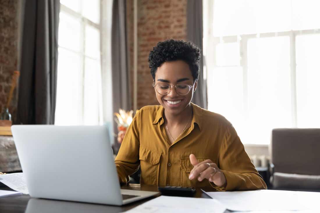 A smiling woman small business owner looks at a list of payments while working on a laptop